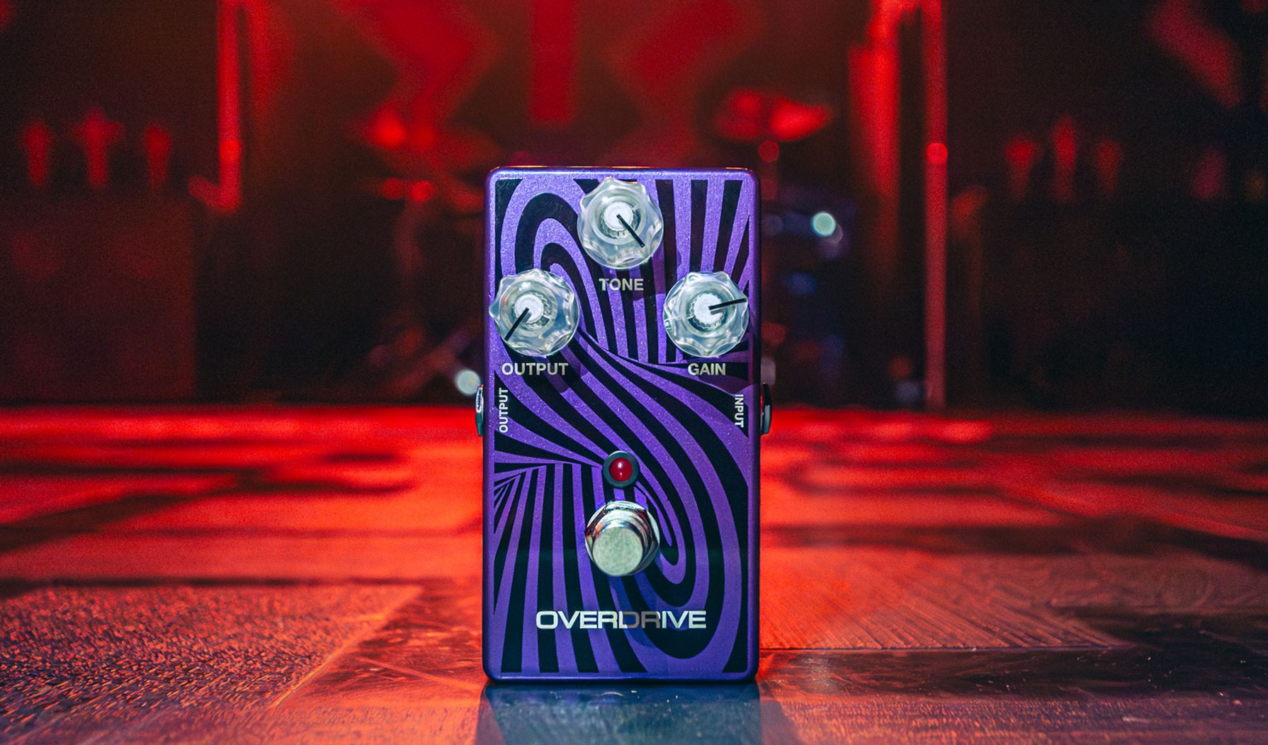 Pédale d’overdrive MXR Wylde Audio Zakk Sabbath violette, avec réglages Output, Tone et Gain, sur une scène éclairée en rouge