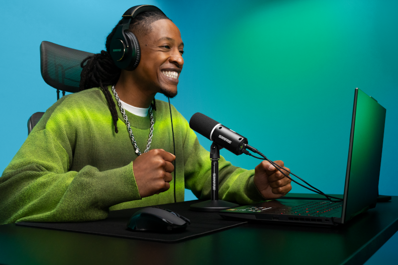 Gamer utilisant le microphone Shure MV6 Gen 2 noir devant un ordinateur portable dans une configuration de jeu et de streaming.