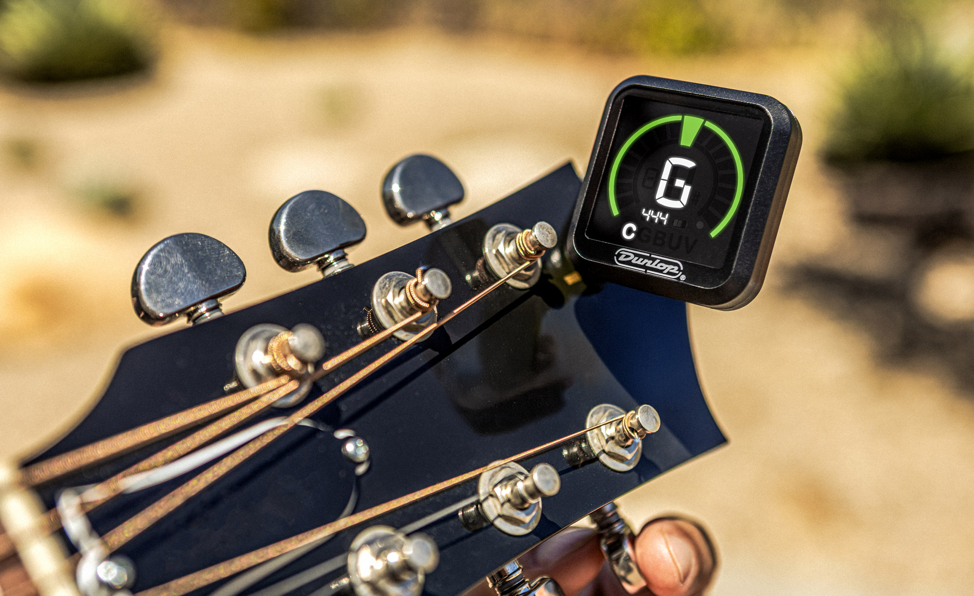 Accordeur clip-on Dunlop fixé sur la tête d’une guitare, affichant une note C sur son écran, avec les mécaniques et les cordes de l’instrument au premier plan.
