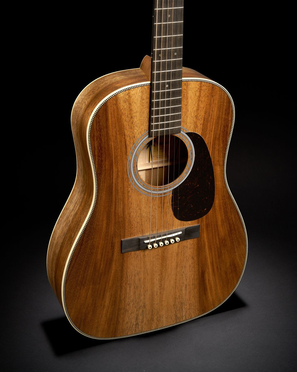 Guitare Martin O’ahu HG-28K2 acoustique à cordes acier avec une table en bois brun aux veines apparentes, sur fond noir.
