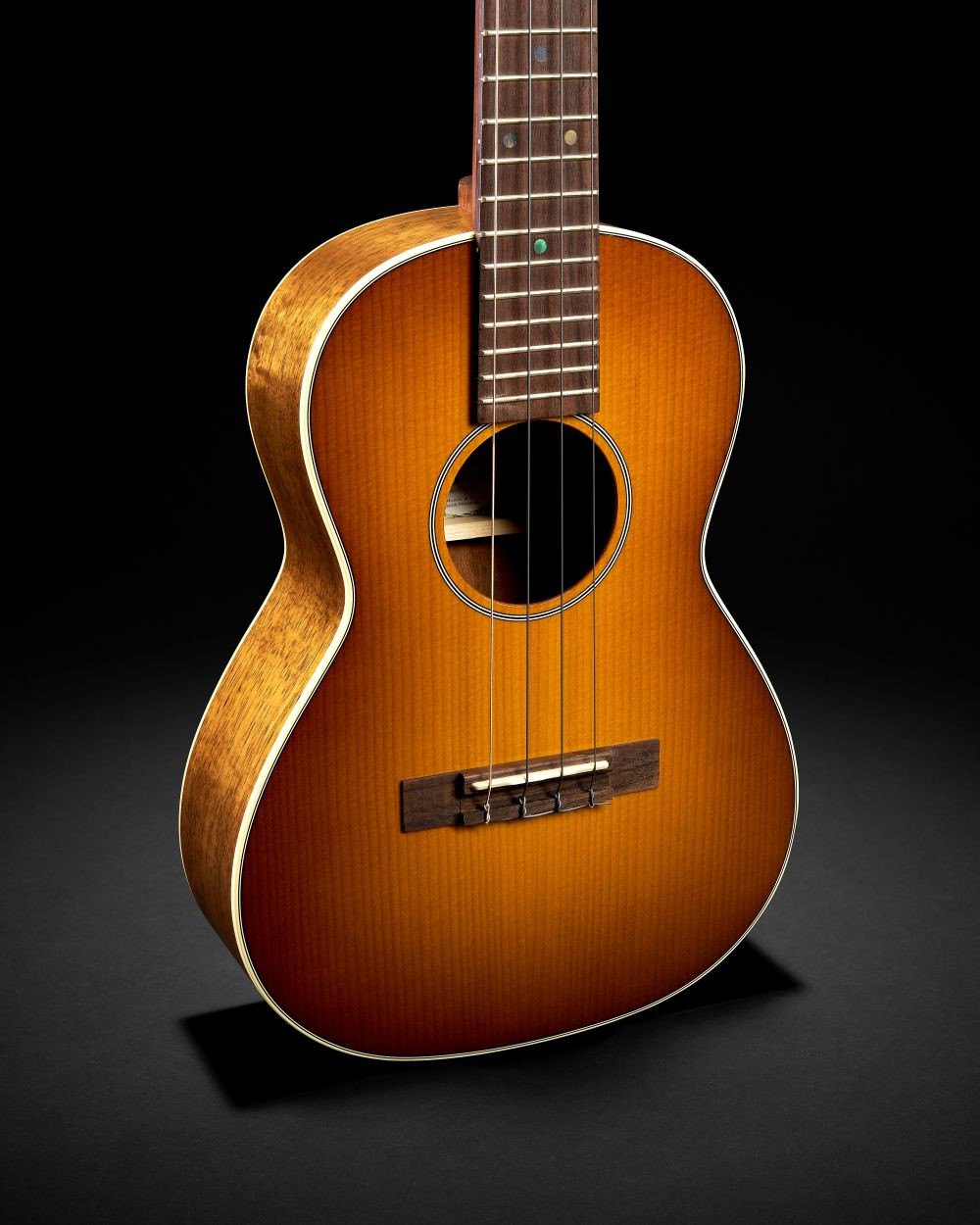 Ukulélé Martin O’ahu TKE Uke Burst avec une finition bois verni en dégradé, présenté sur un fond noir uni.
