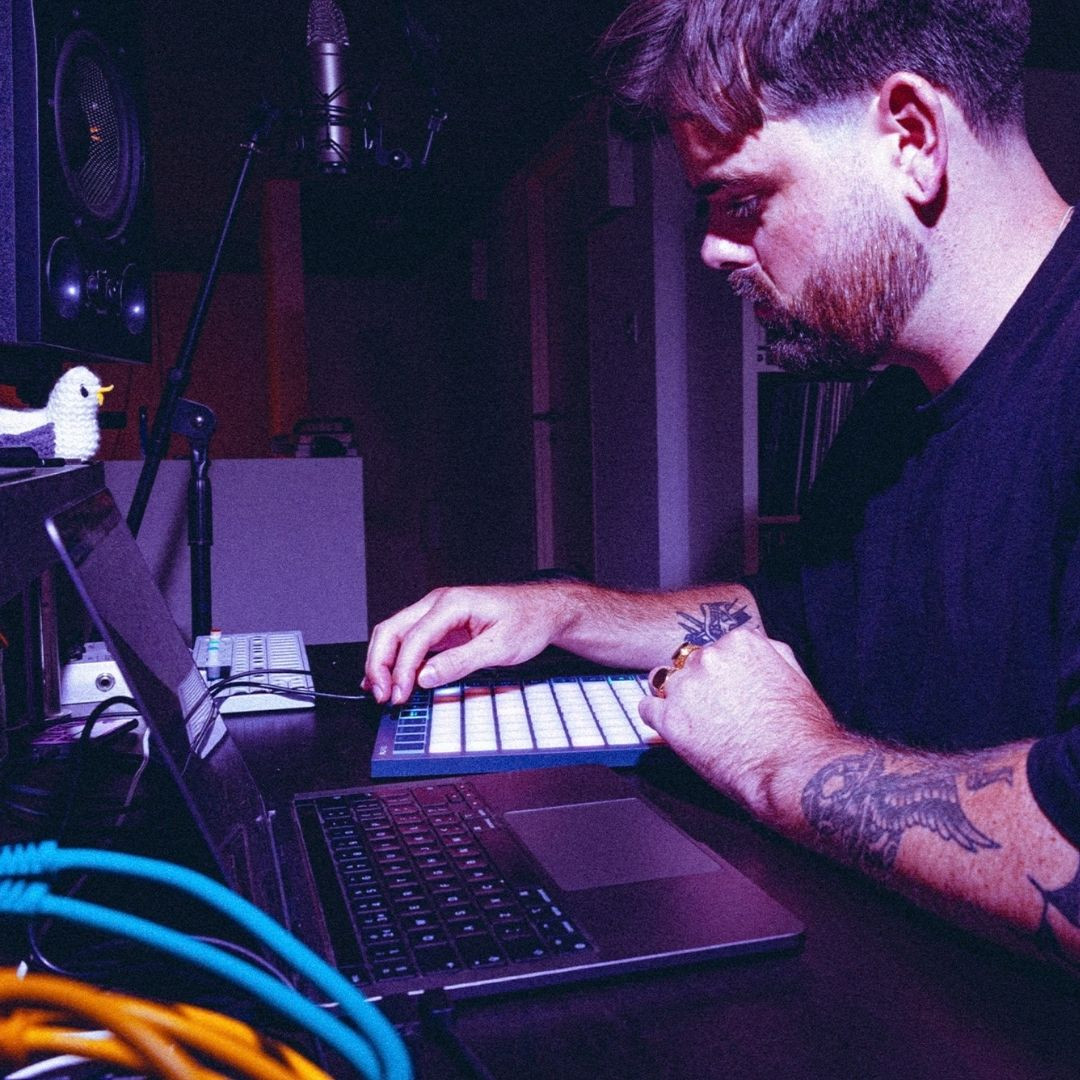 Un producteur de musique utilisant un ordinateur portable et un contrôleur MIDI lumineux pour composer sur un logiciel de production audio