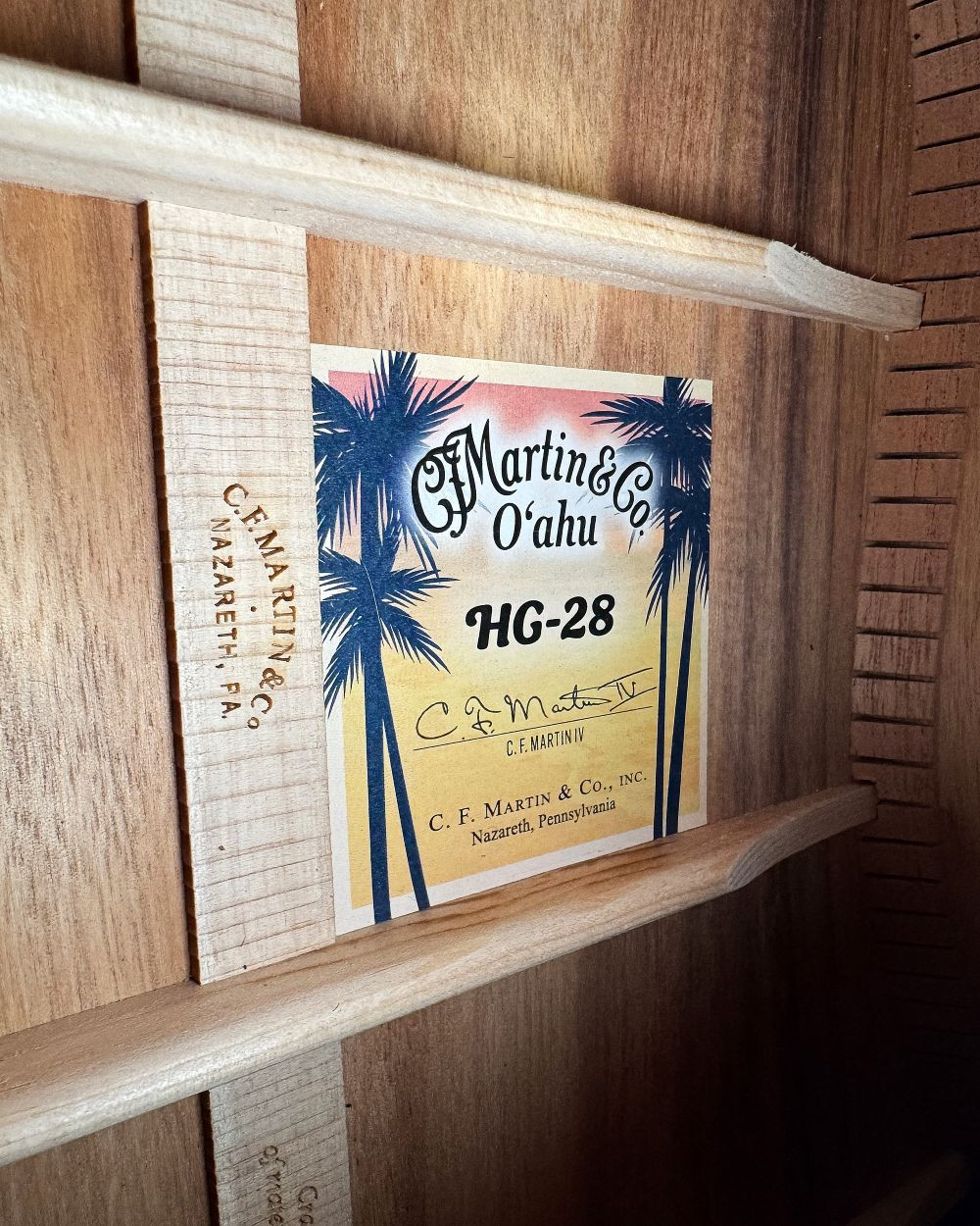 Guitare Martin O’ahu HG-28K2 acoustique à cordes acier avec une table en bois brun aux veines apparentes, sur fond noir.