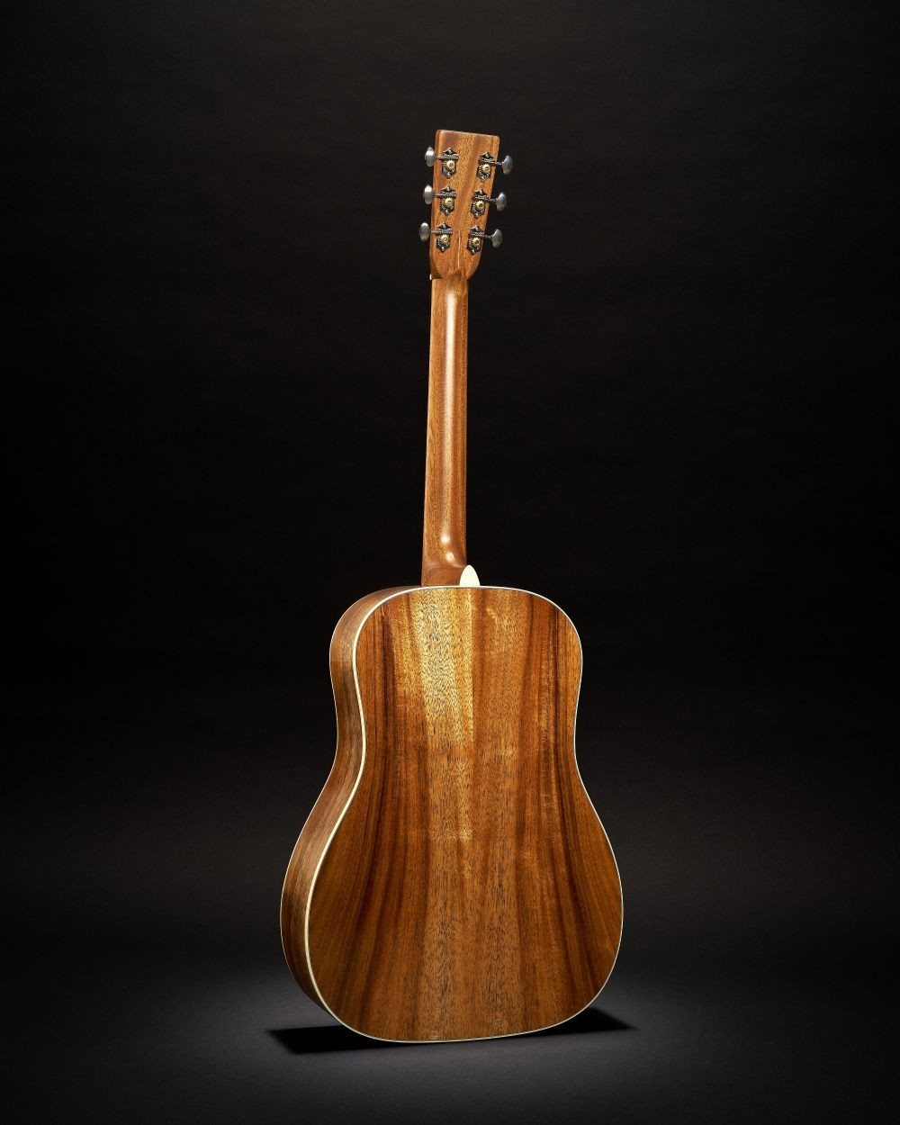 Guitare Martin O’ahu HG-28K2 acoustique à cordes acier avec une table en bois brun aux veines apparentes, vue arrière sur fond noir.